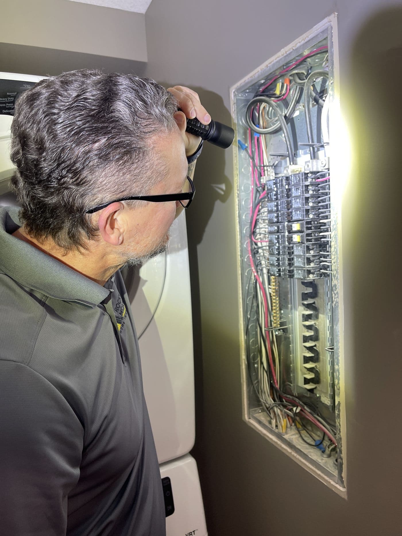 Kyle Dowdeswell inspecting an open electrical panel with a flashlight