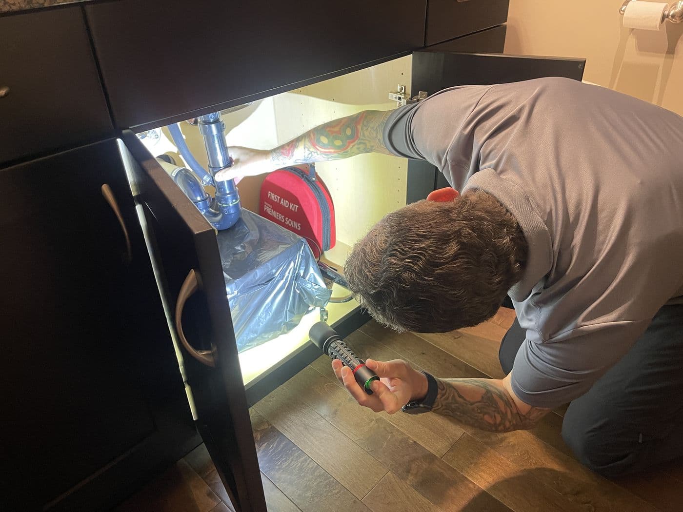Kyle Dowdeswell checking plumbing under a sink with a flashlight