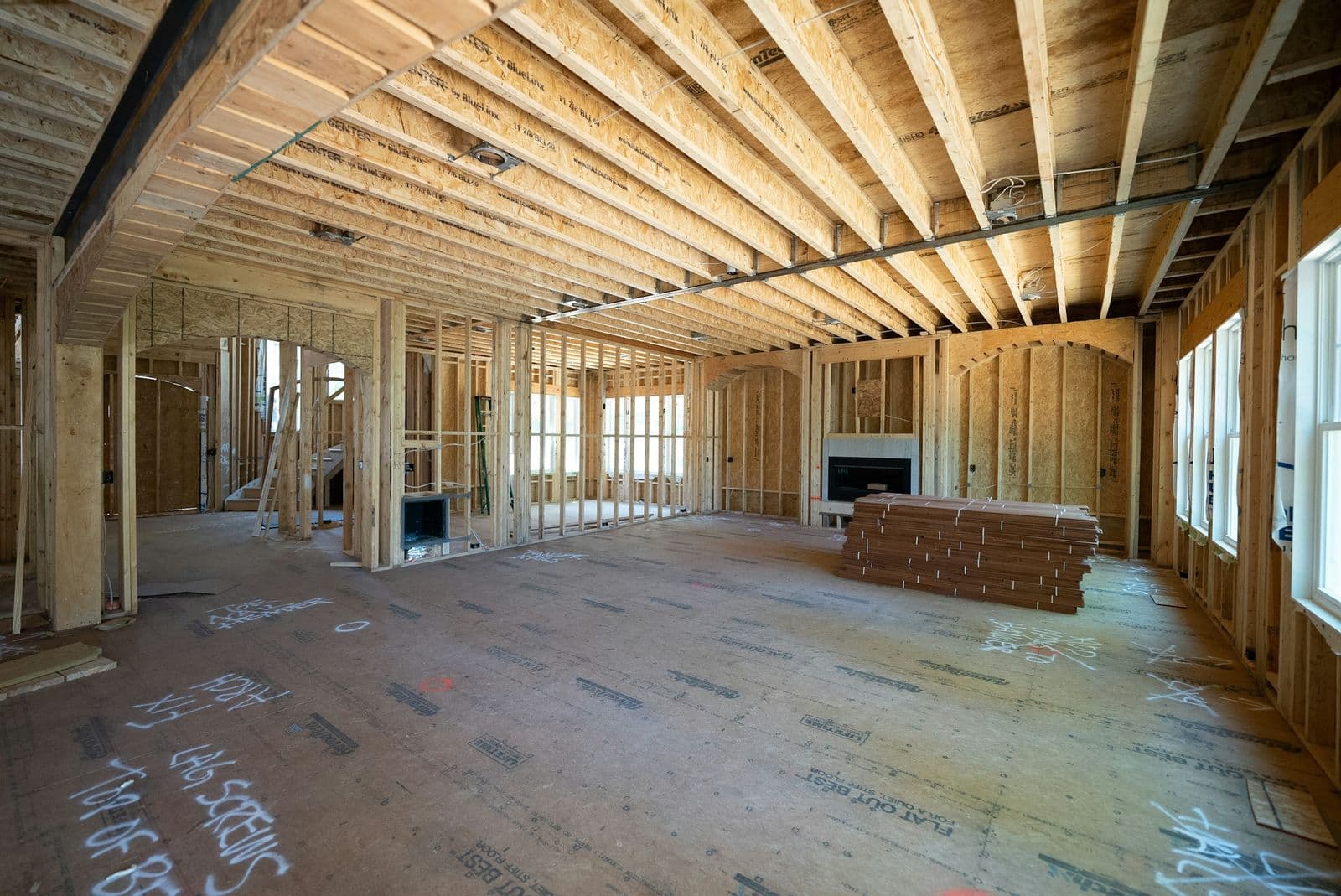 Inside a framed new home before drywall: open wall studs, floor joists overhead and rough-in wiring